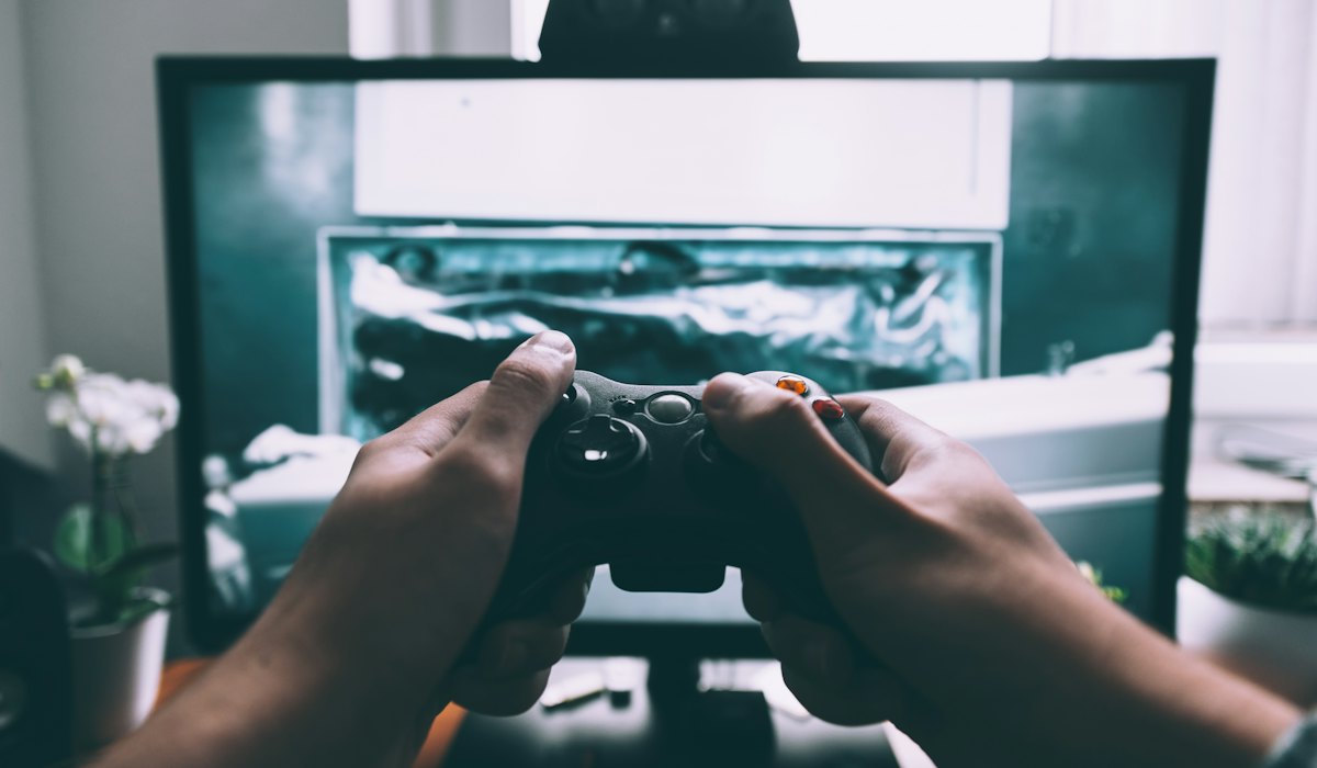 Mãos de um jogador adulto segurando o controle diante da tela