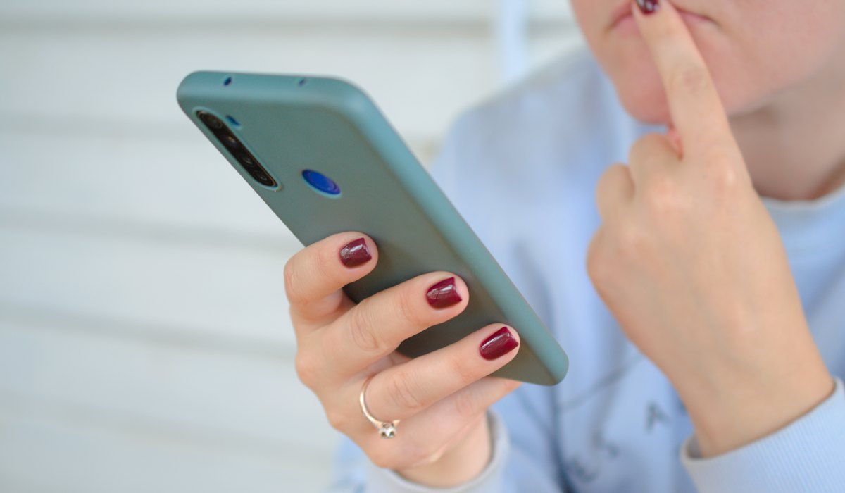 Mão segurando o celular, em dúvida, com o aplicativo de mensagens bloqueado
