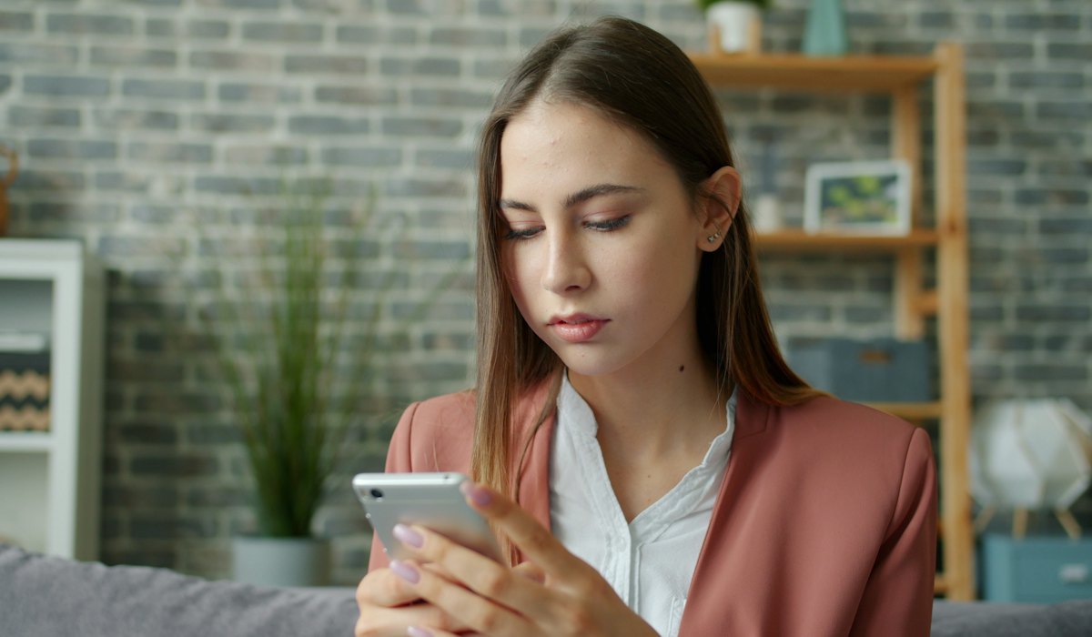 Mulher preocupada olhando o celular, com o perfil suspenso